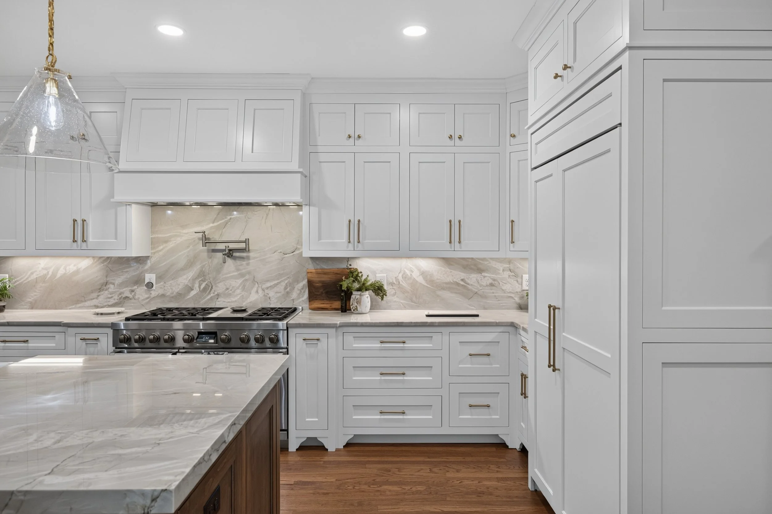 Modern kitchen with white cabinets, marble countertops, a stainless steel stove, and a glass pendant light.