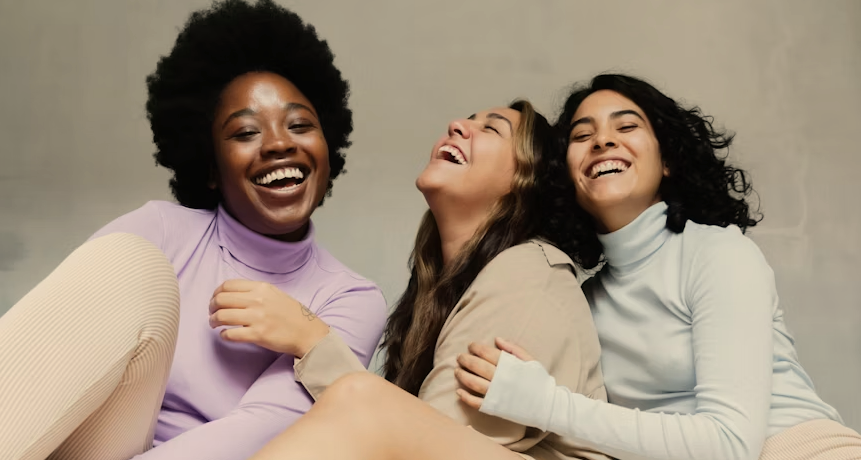 Three women laughing and sitting close together, showing friendship and happiness.