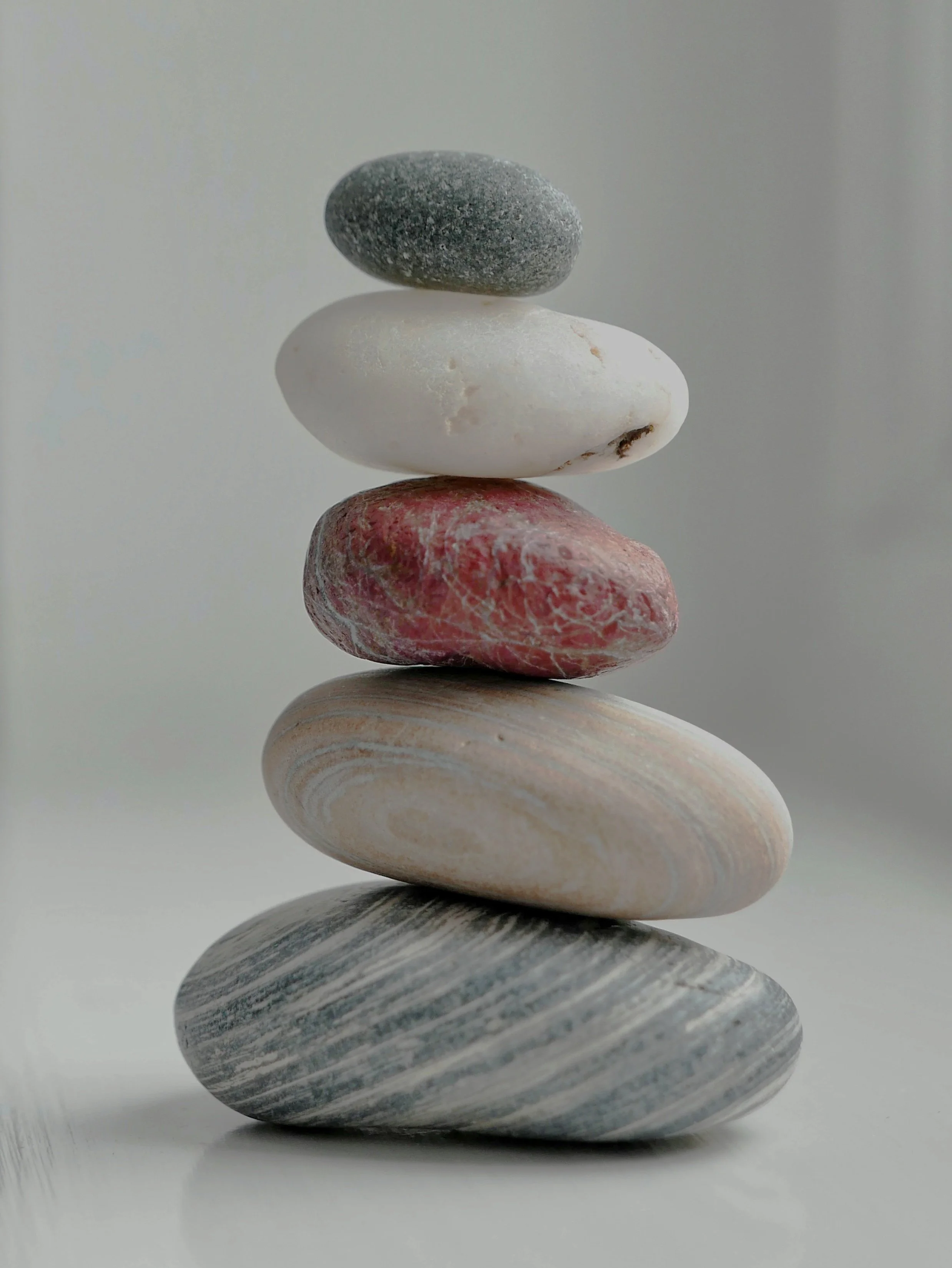 Stack of six smooth, flat stones in different colors and patterns, arranged in a balanced tower against a white background.