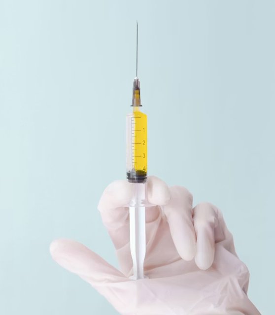 A gloved hand holding a syringe filled with yellow liquid against a plain, light blue background.