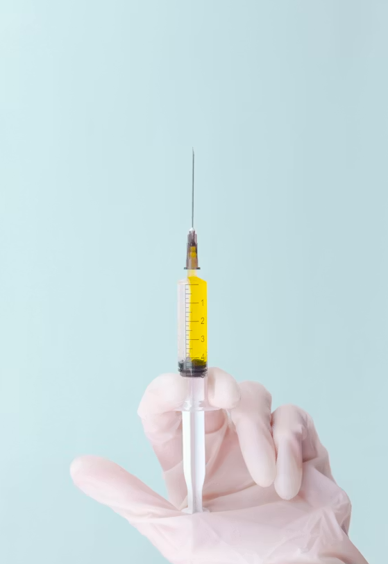 A gloved hand holding a syringe filled with yellow liquid, against a light blue background.