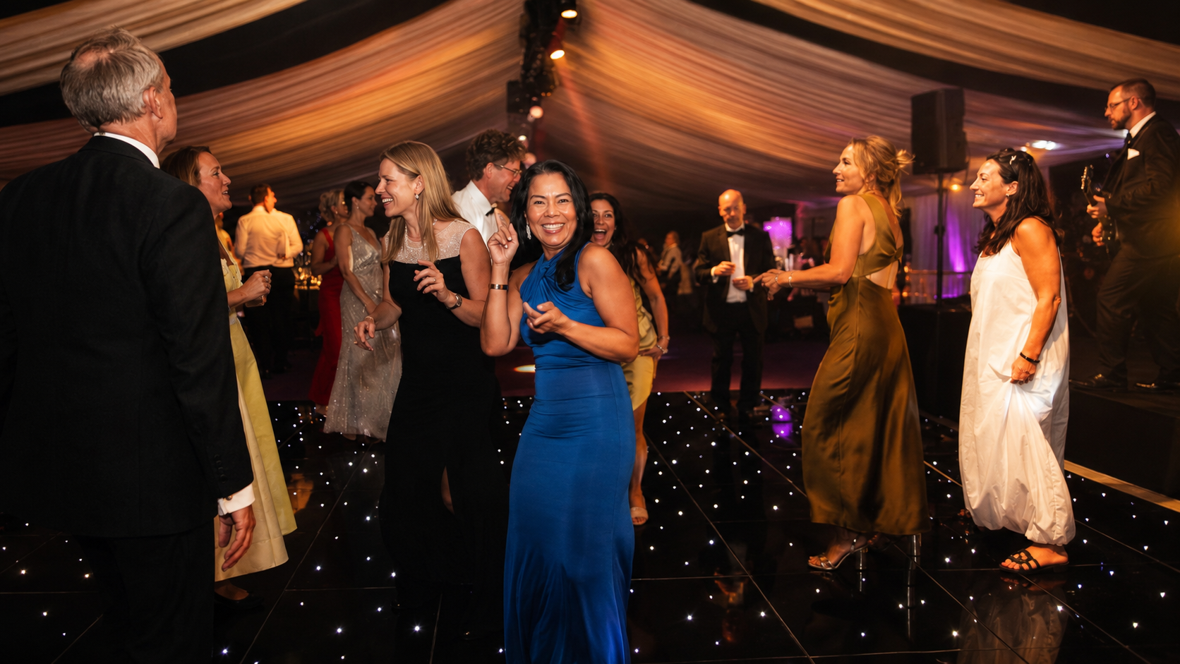 Guests dancing on a lit dance floor while Revolve Party Band performs at a marquee reception
