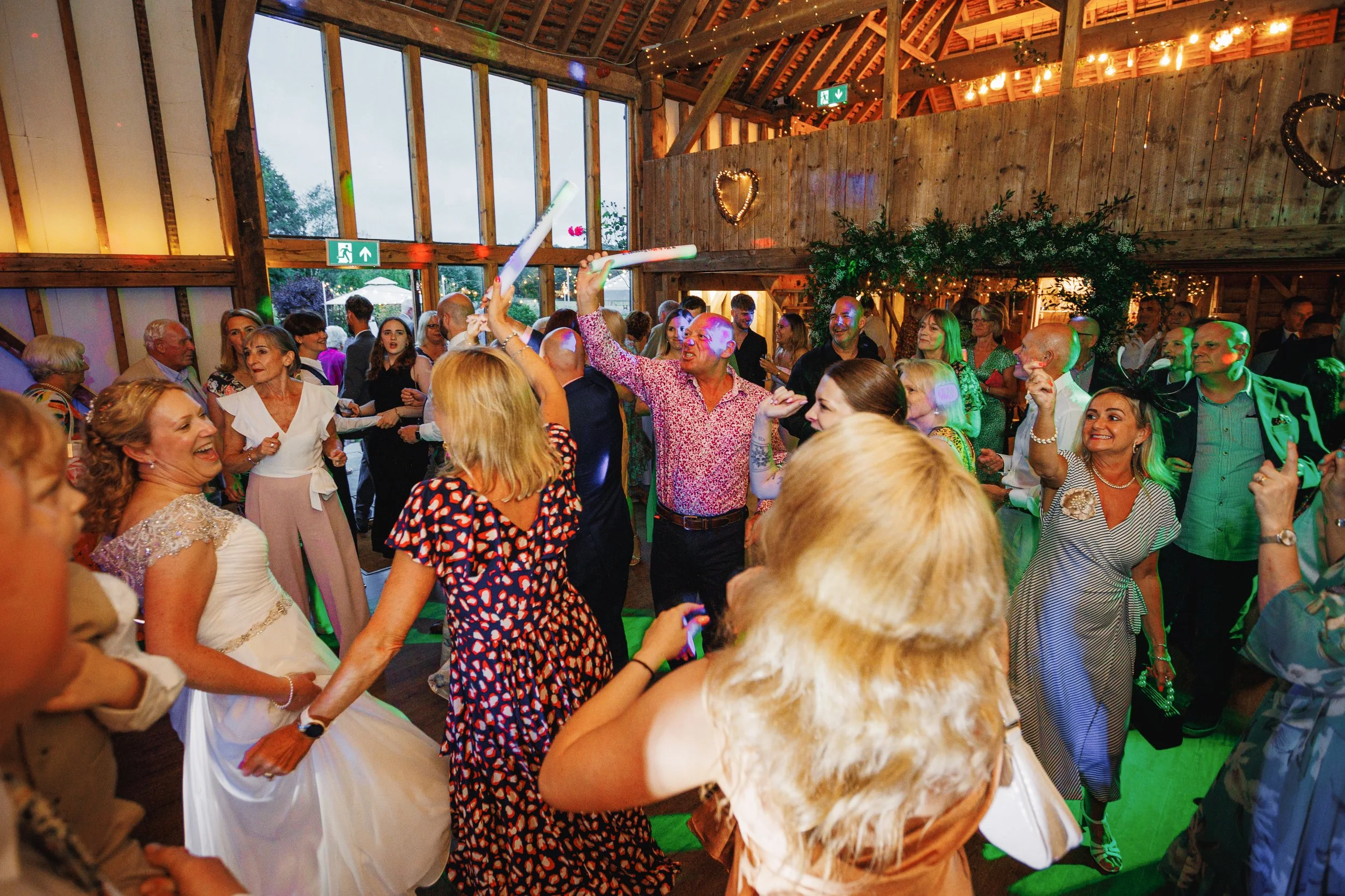 A lively indoor party with people dancing and celebrating, decorated with string lights and heart-shaped ornaments.