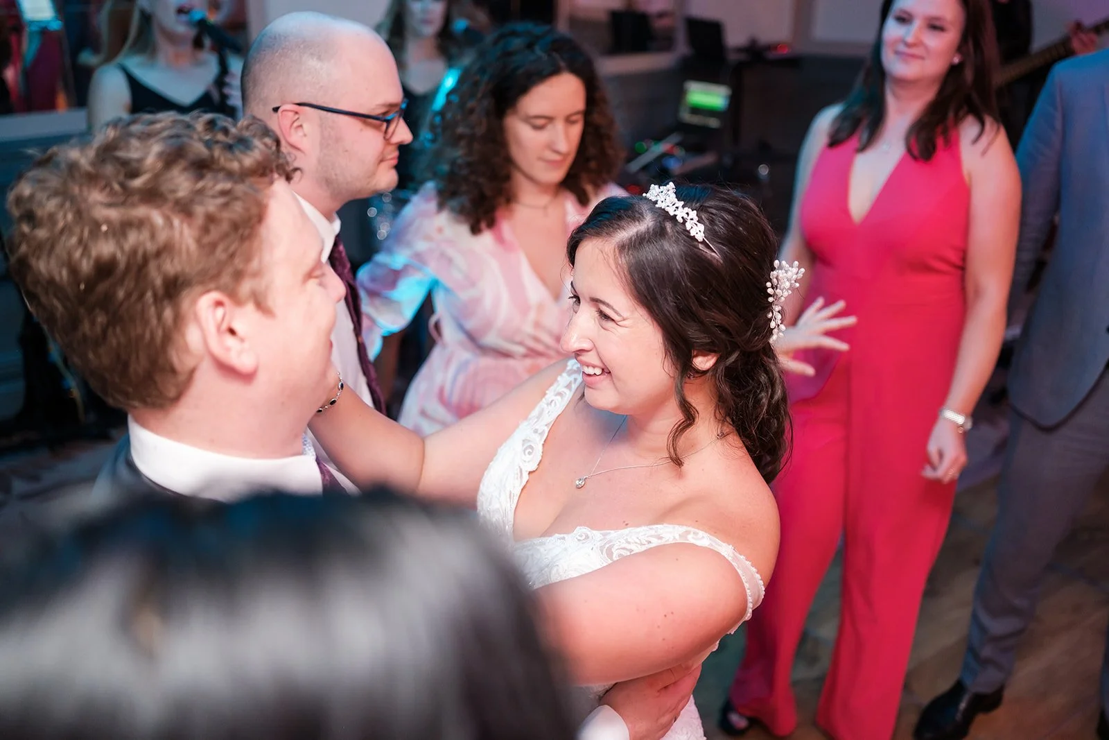 A bride and groom dancing together during a wedding reception, smiling at each other surrounded by guests.