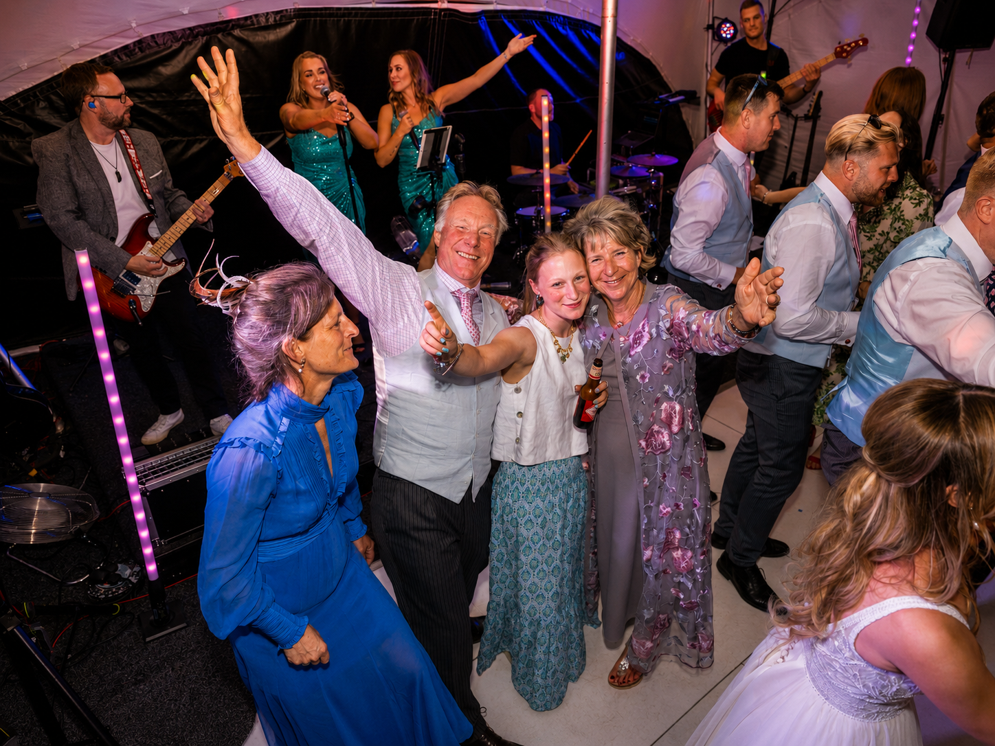 People dancing at a lively celebration with a band playing on stage in the background.