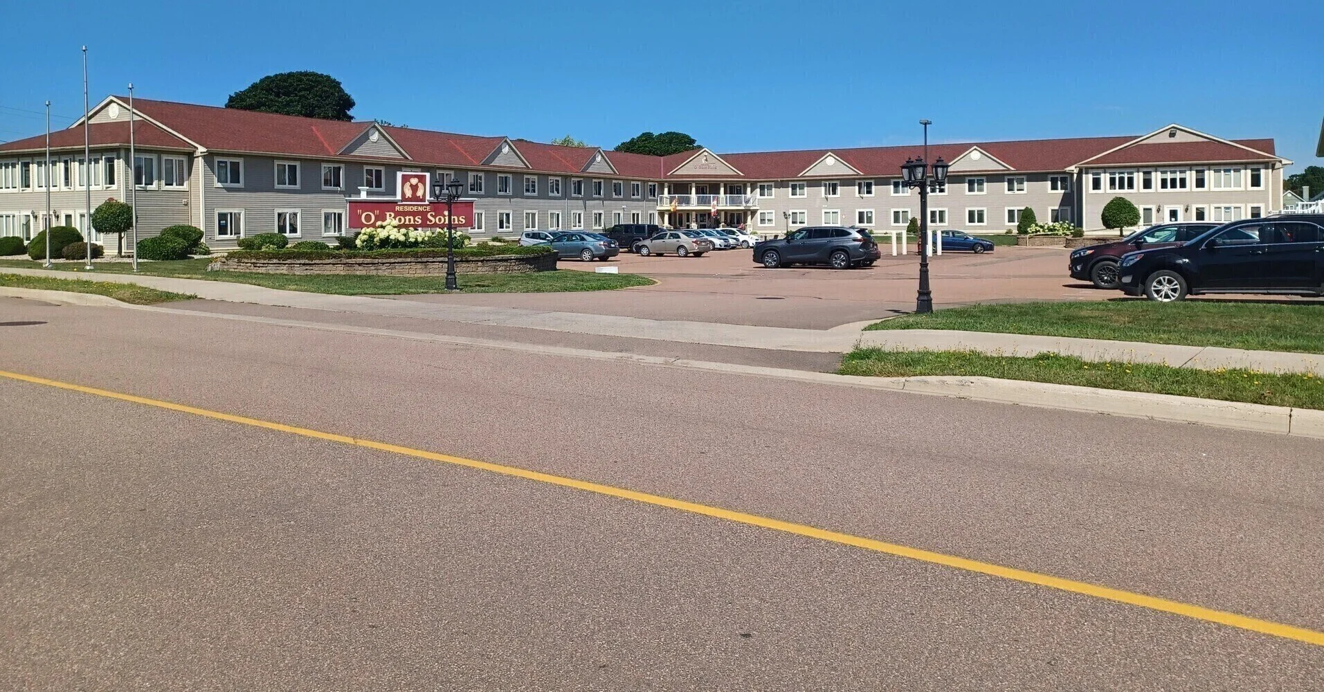 A large residential building with a parking lot in front, cars parked, and a sign that reads 'O' Bons Soins'