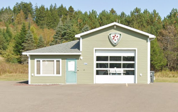 Small ambulance station building with a large garage door, a side door, and a sign with a red cross emblem on the front