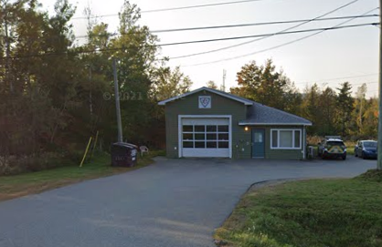 A fire station with a garage door, a small window, and a parked vehicle in a suburban area.
