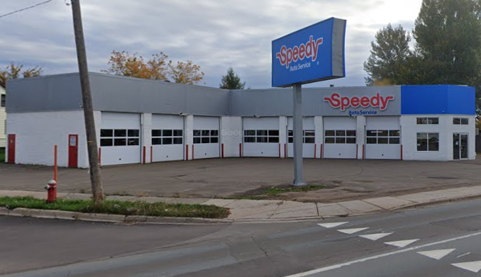 Speedy auto service garage with a large blue sign and a building with multiple garage bays, situated on a street with a crosswalk.