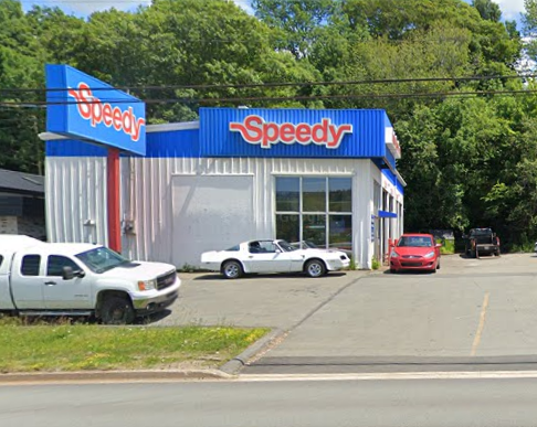 Speedy auto repair shop with a blue and red sign, several parked cars in front, and a wooded background.