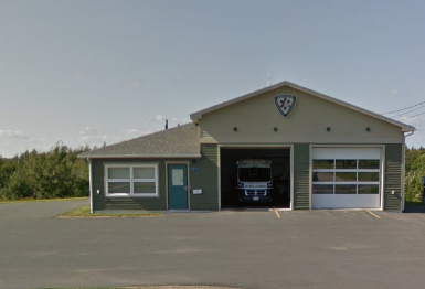 A fire station with a truck parked inside the garage, located in a parking lot with trees in the background.