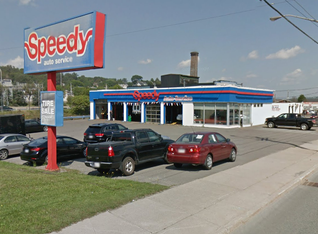 Speedy auto service building with a large sign, vehicles parked in the lot, and a sign indicating a tire sale.