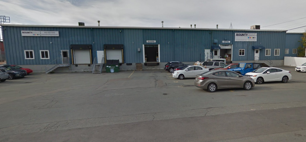 Exterior view of a large warehouse building with a parking lot filled with cars.