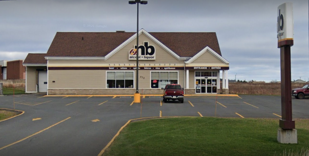 A single-story liquor store with a large sign reading 'hb alcohol + liquor', parking lot with a few parked cars, and a sign post on the right side of the image, under a cloudy sky.
