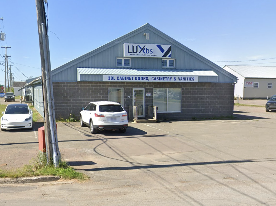 Building with a sign that reads 'LUX bs' and another sign that says '3DL Cabinet Doors, Cabinetry & Vanities.' Parking lot with a few cars parked in front.