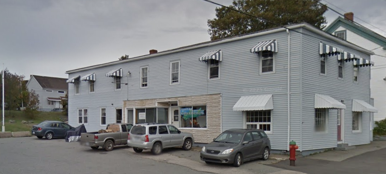 A two-story building with light blue siding, striped awnings over the windows, parked cars in front, and a fire hydrant on the sidewalk.