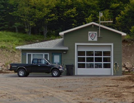A green garage with a large glass door, a smaller side door, and a Sheriff badge emblem above the garage door, with a black pickup truck parked outside.