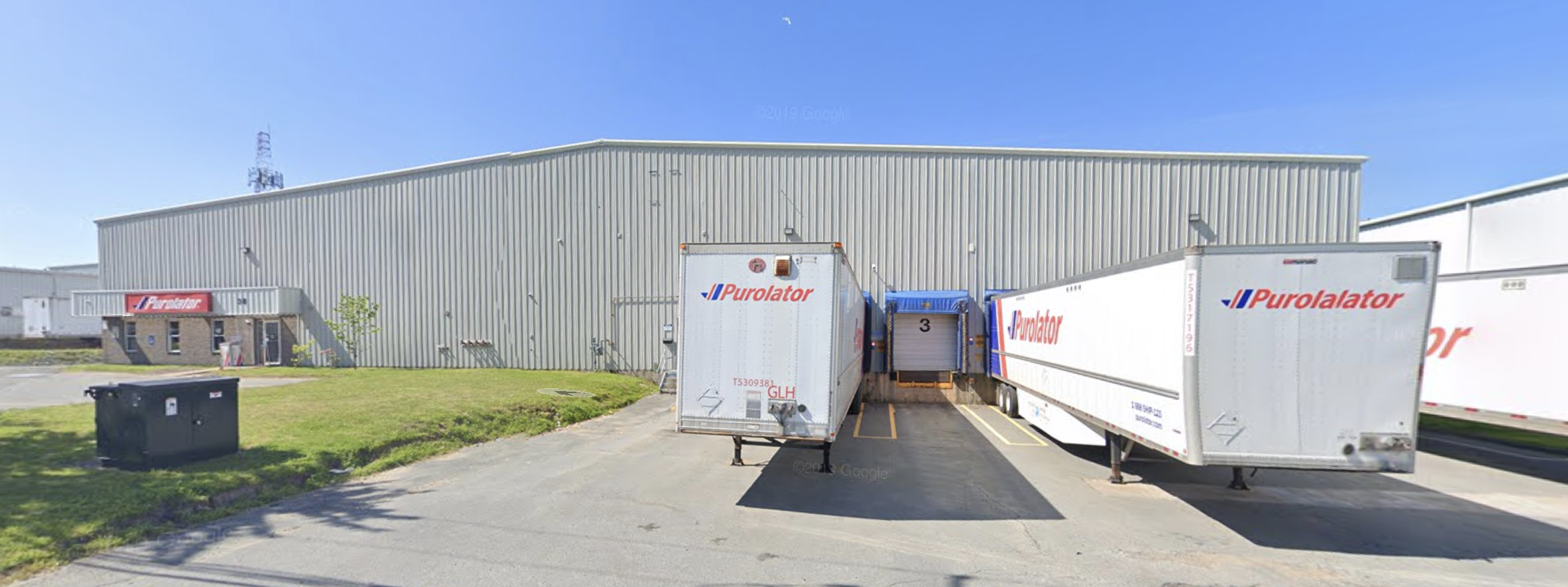 Large industrial building with Purolator delivery trucks parked outside, on a clear day.