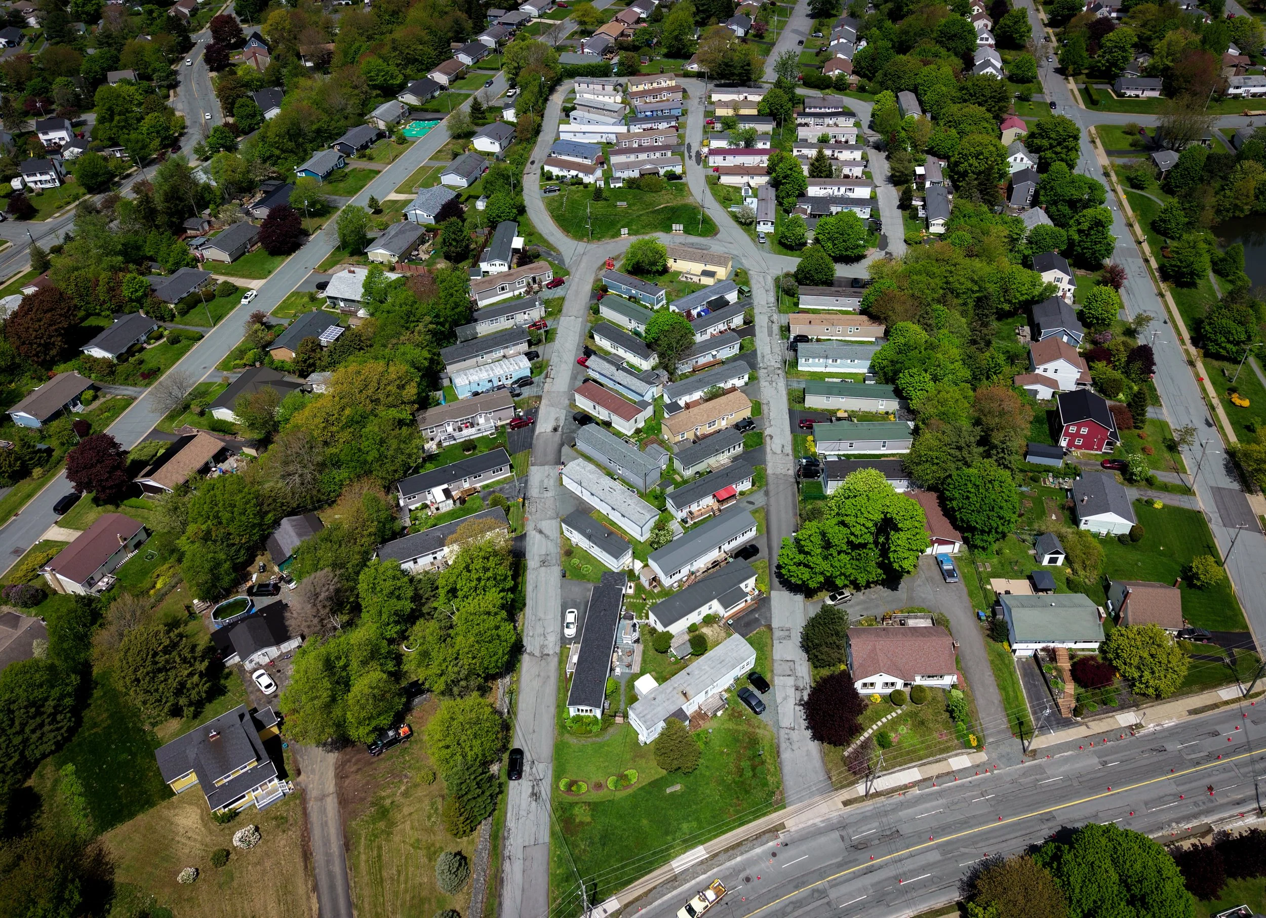 An aerial view of a residential neighborhood with houses, trees, roads, and a swimming pool.