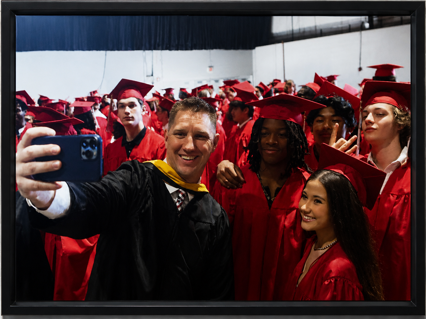 People in red graduation gowns and caps taking a group selfie at a graduation ceremony.