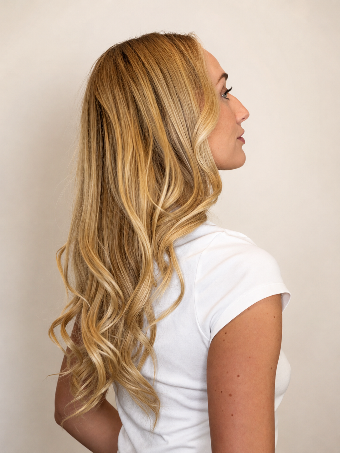 Woman with long blonde extensions showcasing a luxury blowout, against a plain background.
