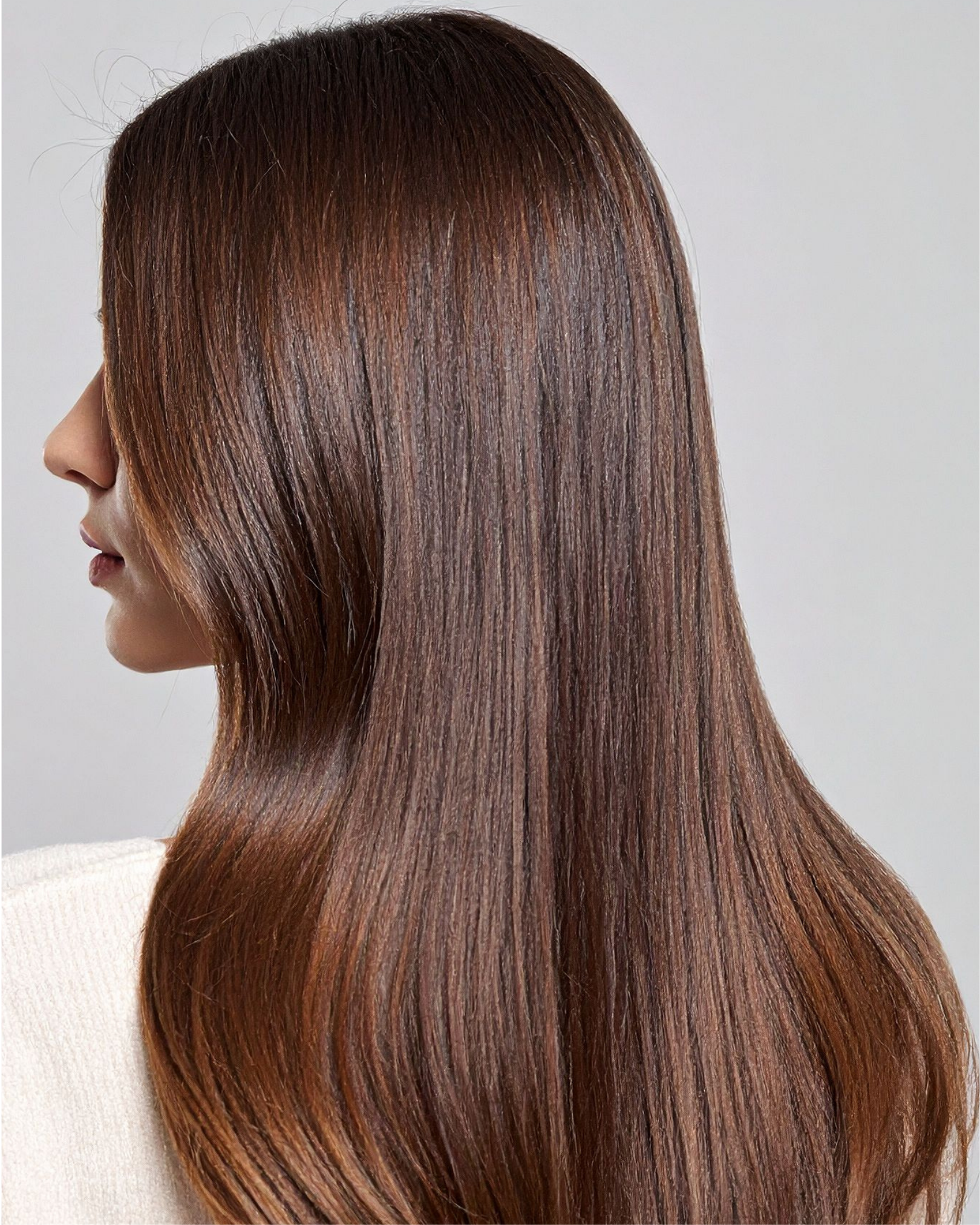 Person with a long, straight, shiny hair  blowout shown from the back and side against a neutral background.