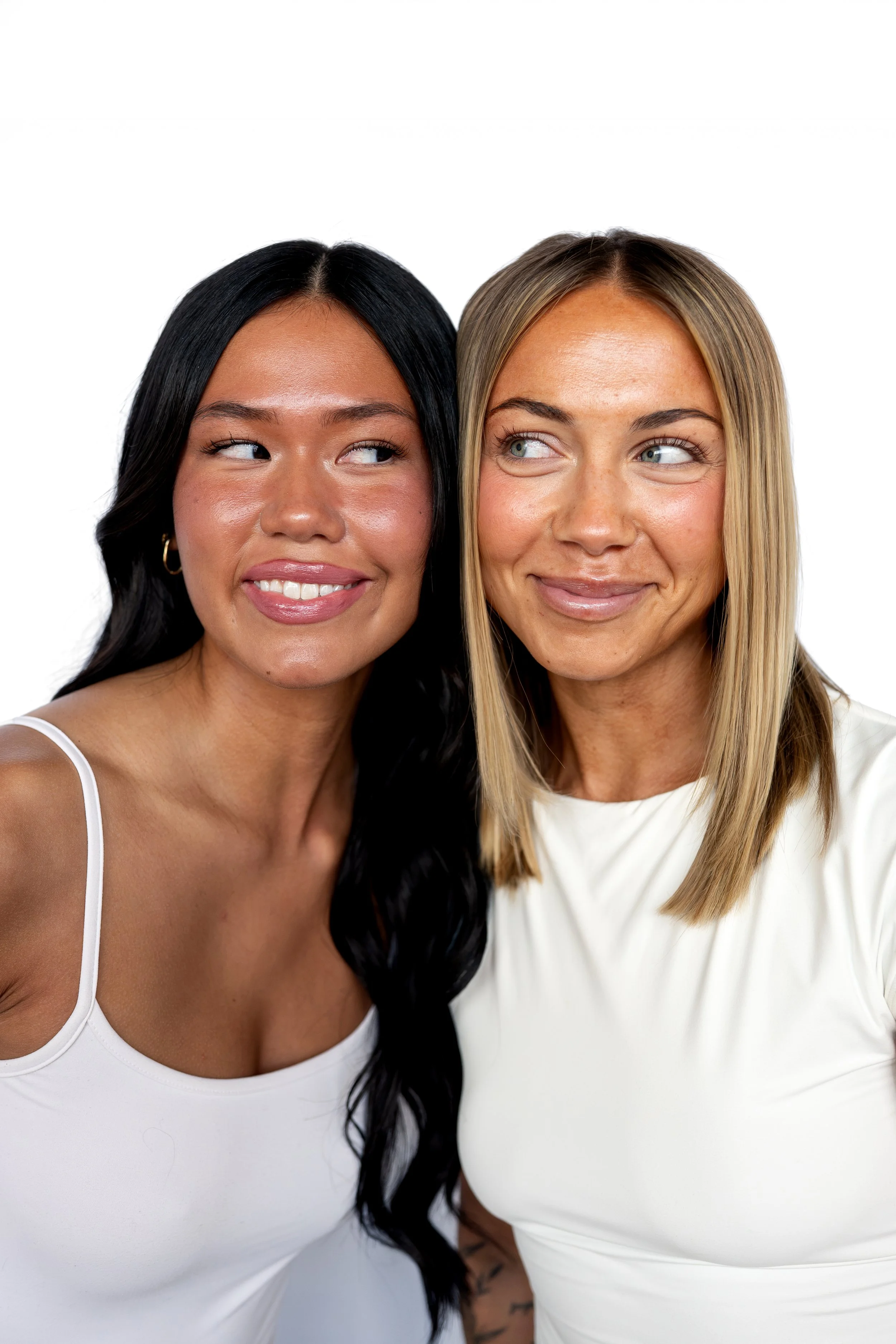 Two women standing close together, smiling and looking at each other against a white background promoting a Niles Ohio hair salon membership.