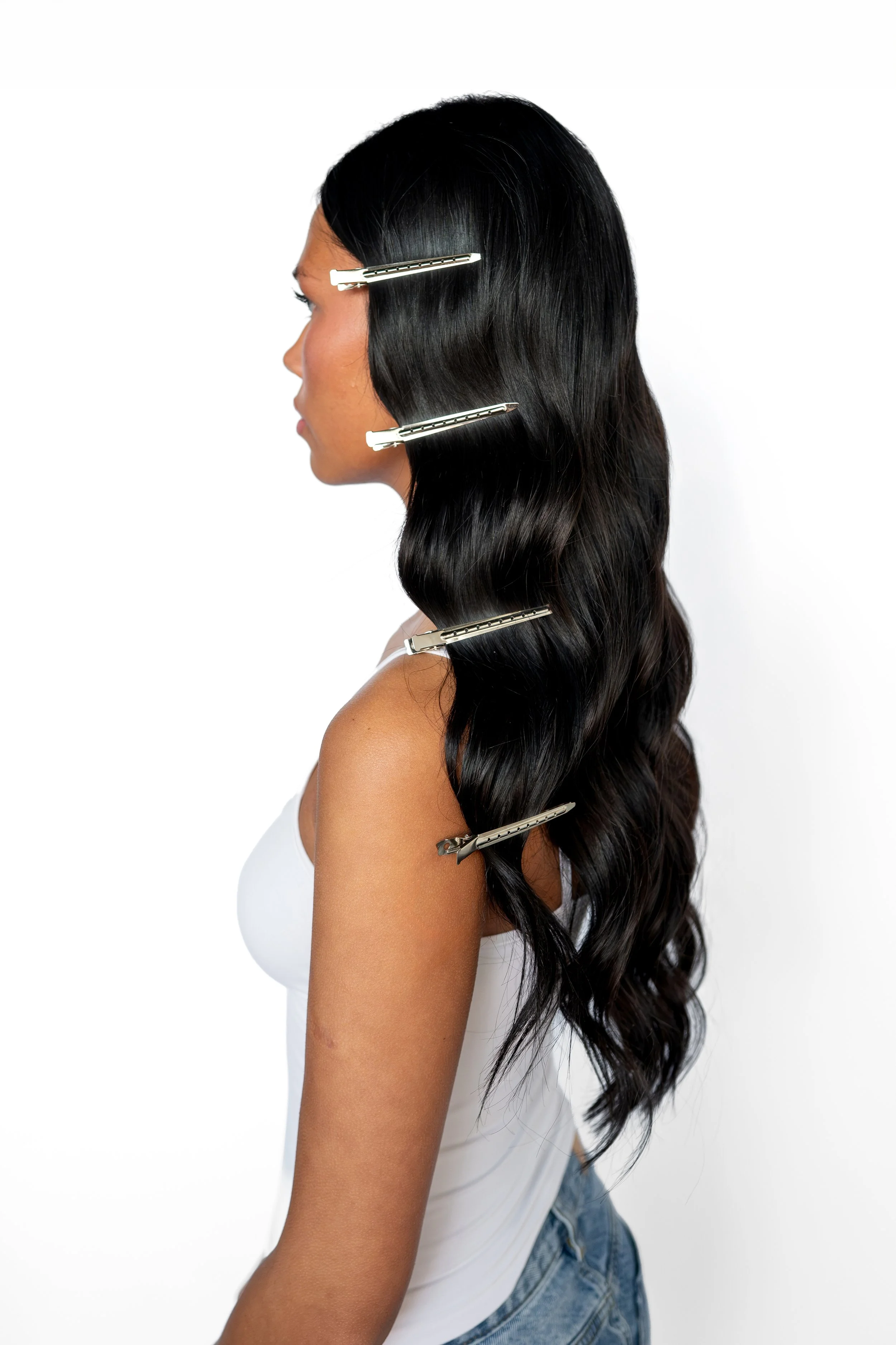 A woman with long wavy dry styled hair for an event, uses sectioning clips on one side, wearing a white tank top.