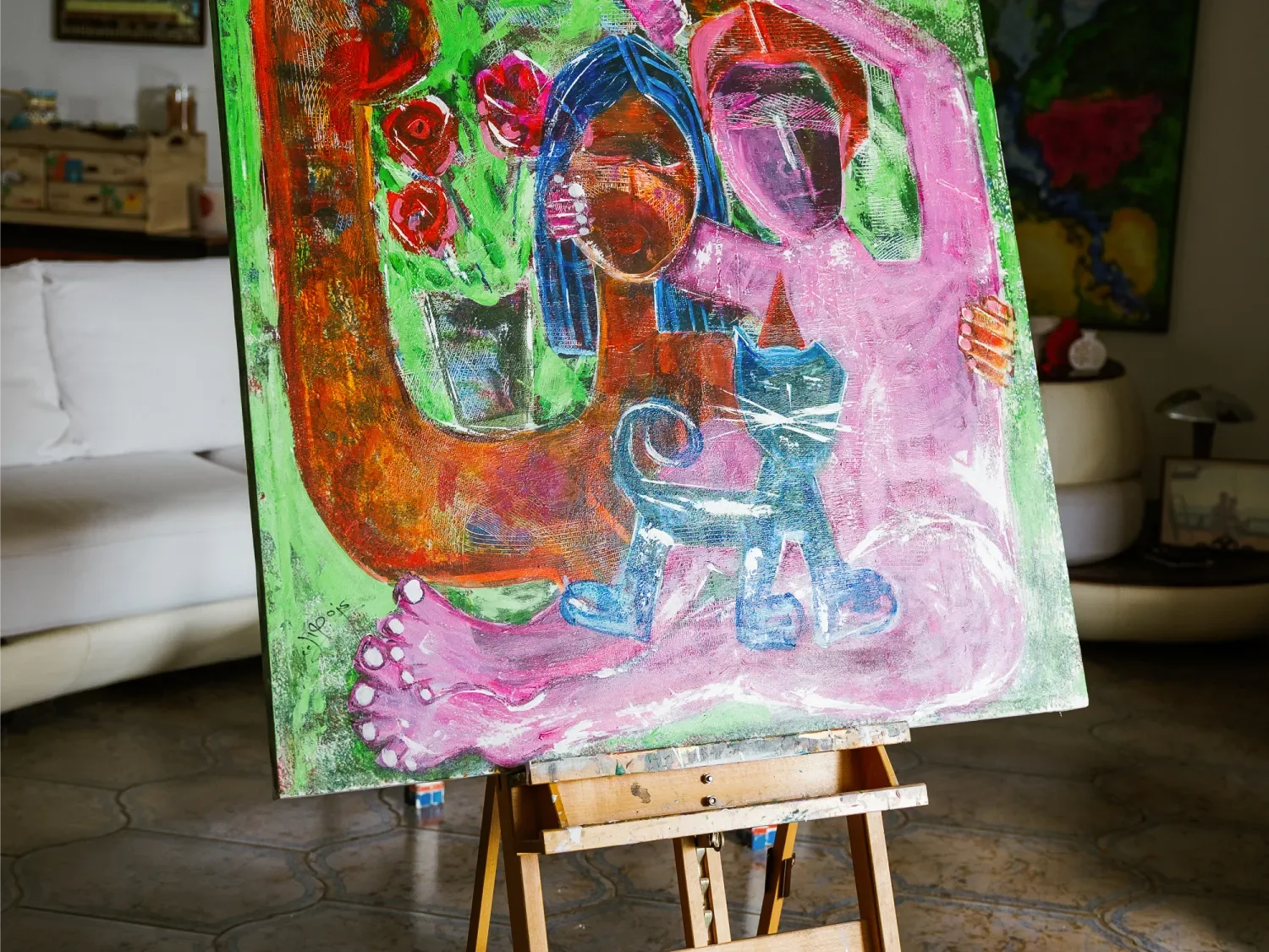 Colorful abstract painting depicting two women, one with blue hair and the other in pink, surrounded by floral and decorative elements, on an easel in a living room.