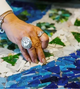 Close-up of a hand with rings arranging colorful mosaic tiles on a surface.