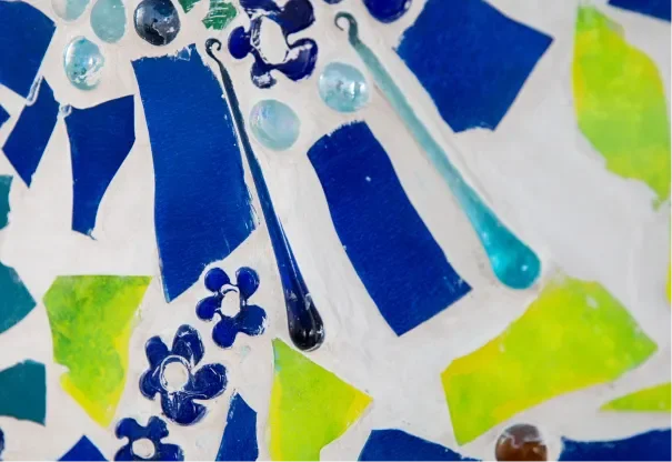 Close-up of colorful painted pieces, including blue, green, and yellow shapes, with some small decorative elements like beads or dots.