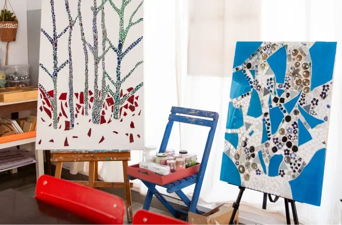Two mosaic canvas paintings on easels in an art studio.