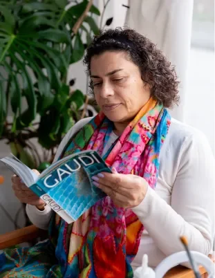 Artist Azza reading a Gaudí book surrounded by plants at Romã Studio