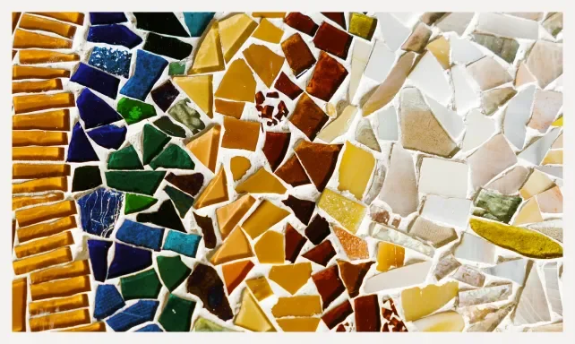 A colorful mosaic composed of broken ceramic tiles in shades of yellow, brown, white, green, blue, and black arranged in vertical strips.