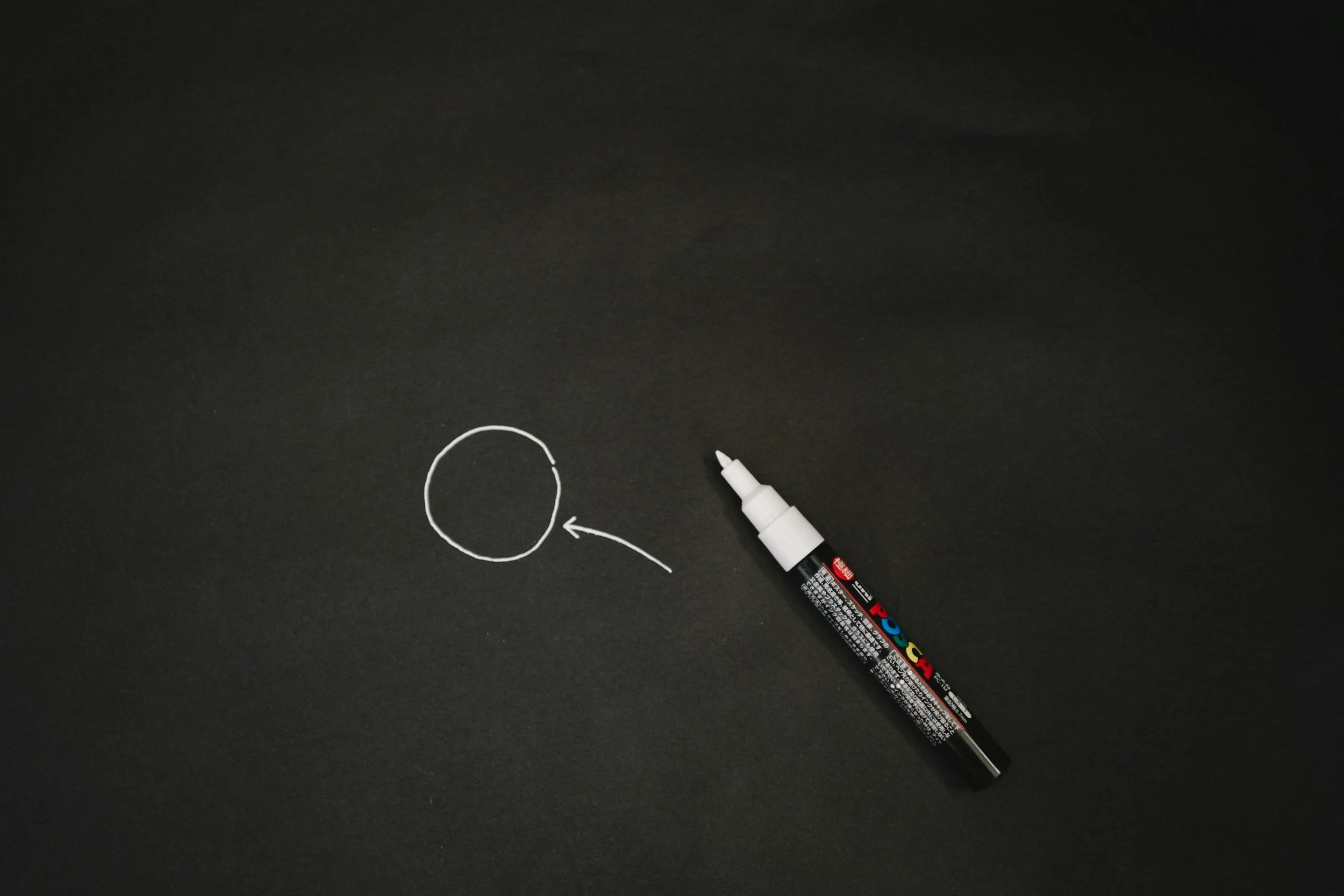 A black chalkboard with a white marker. There is a white circle and an arrow pointing at it drawn on the chalkboard.
