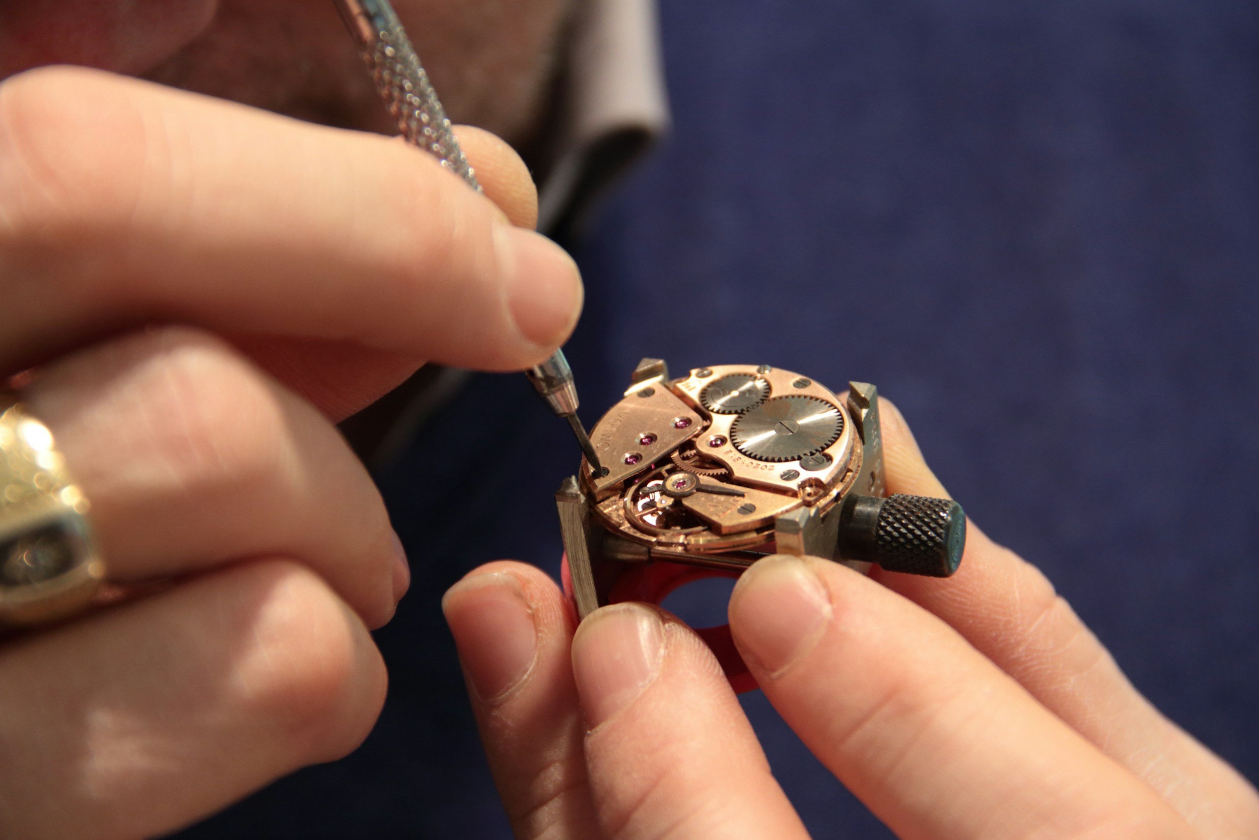A person is using a small screwdriver to work on the inner mechanism of a watch, with their fingers steadying the watch case.