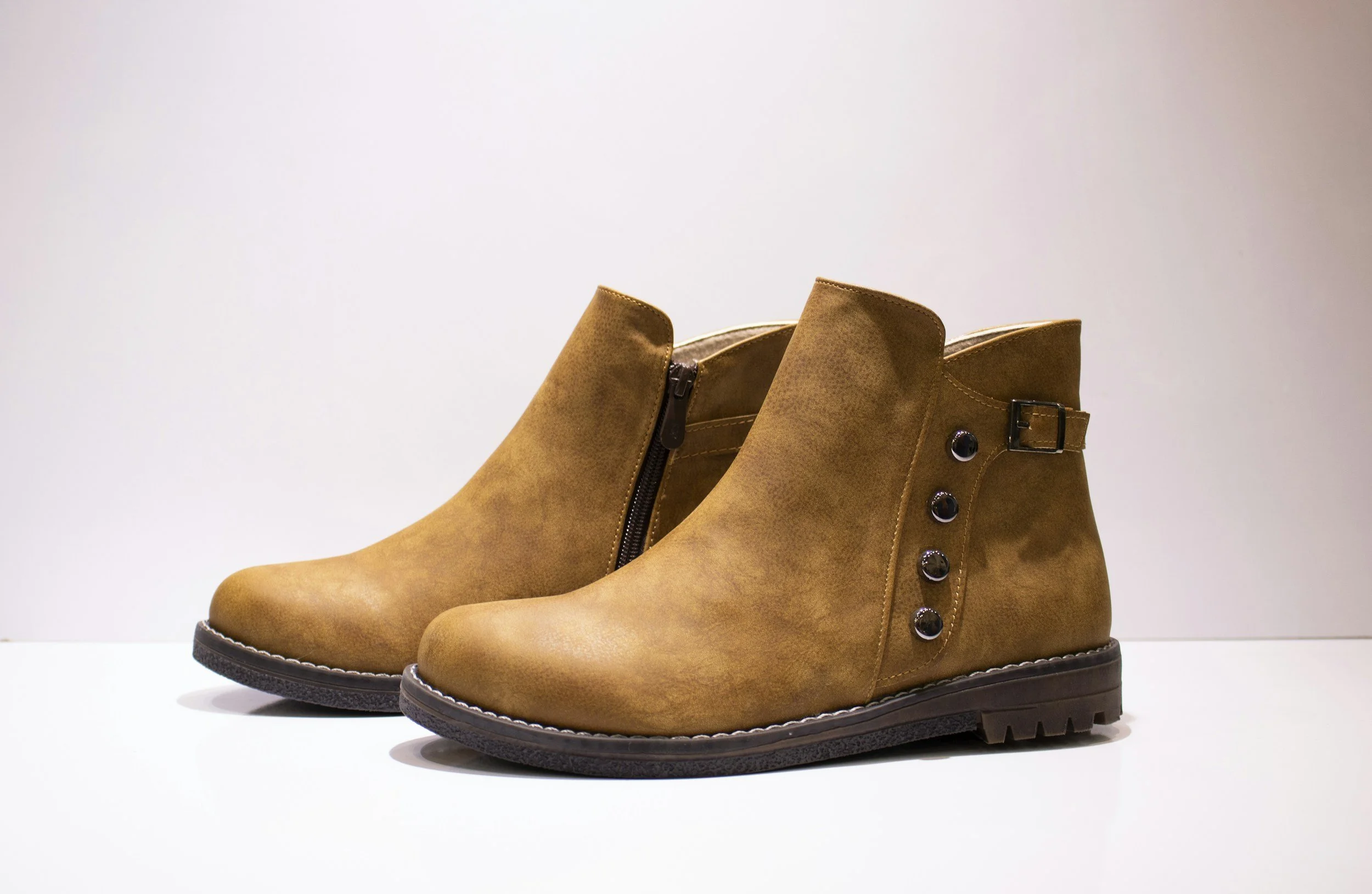 A pair of tan leather ankle boots with black soles, silver cirque eyelet accents, and zippers on the inner sides, displayed against a white background.