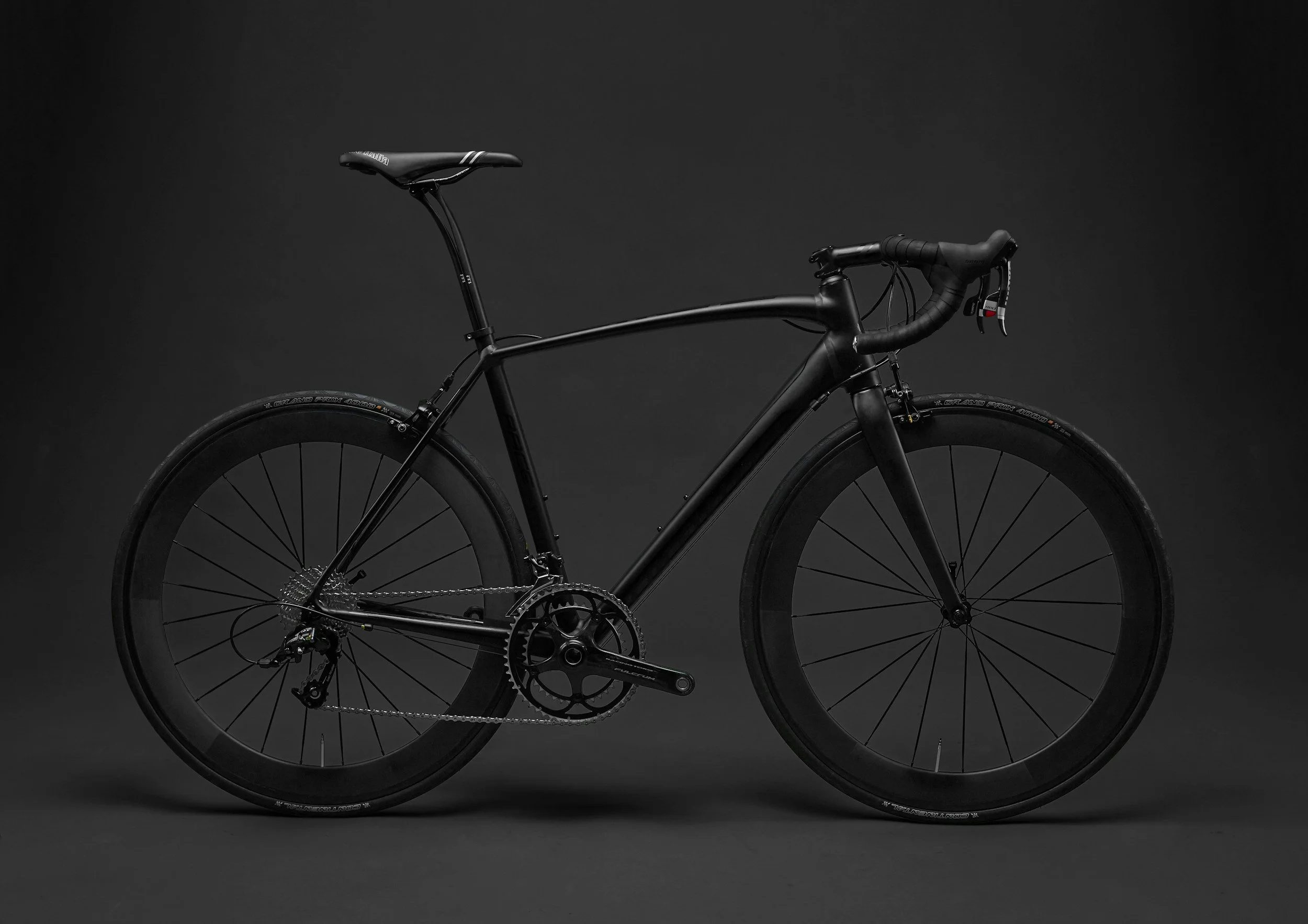 Black road bicycle against a dark background, showcasing sleek frame, drop handlebars, and large tires.