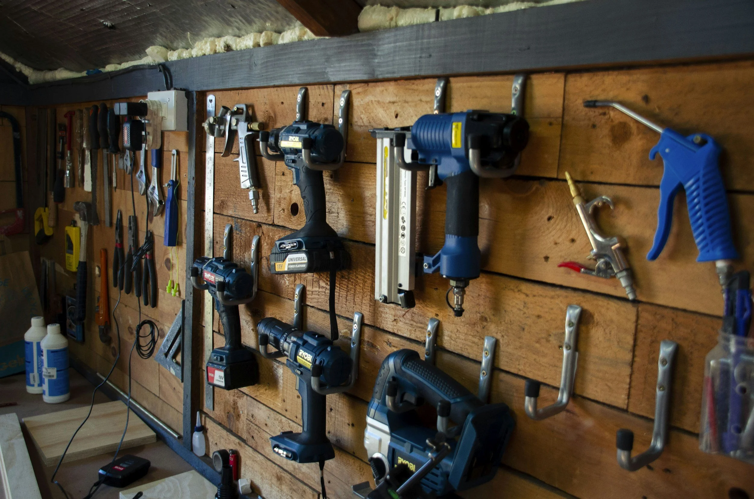 A wooden workbench mounted with various power tools and hand tools, including drills, saws, clamps, and screwdrivers, organized in a workshop setting.