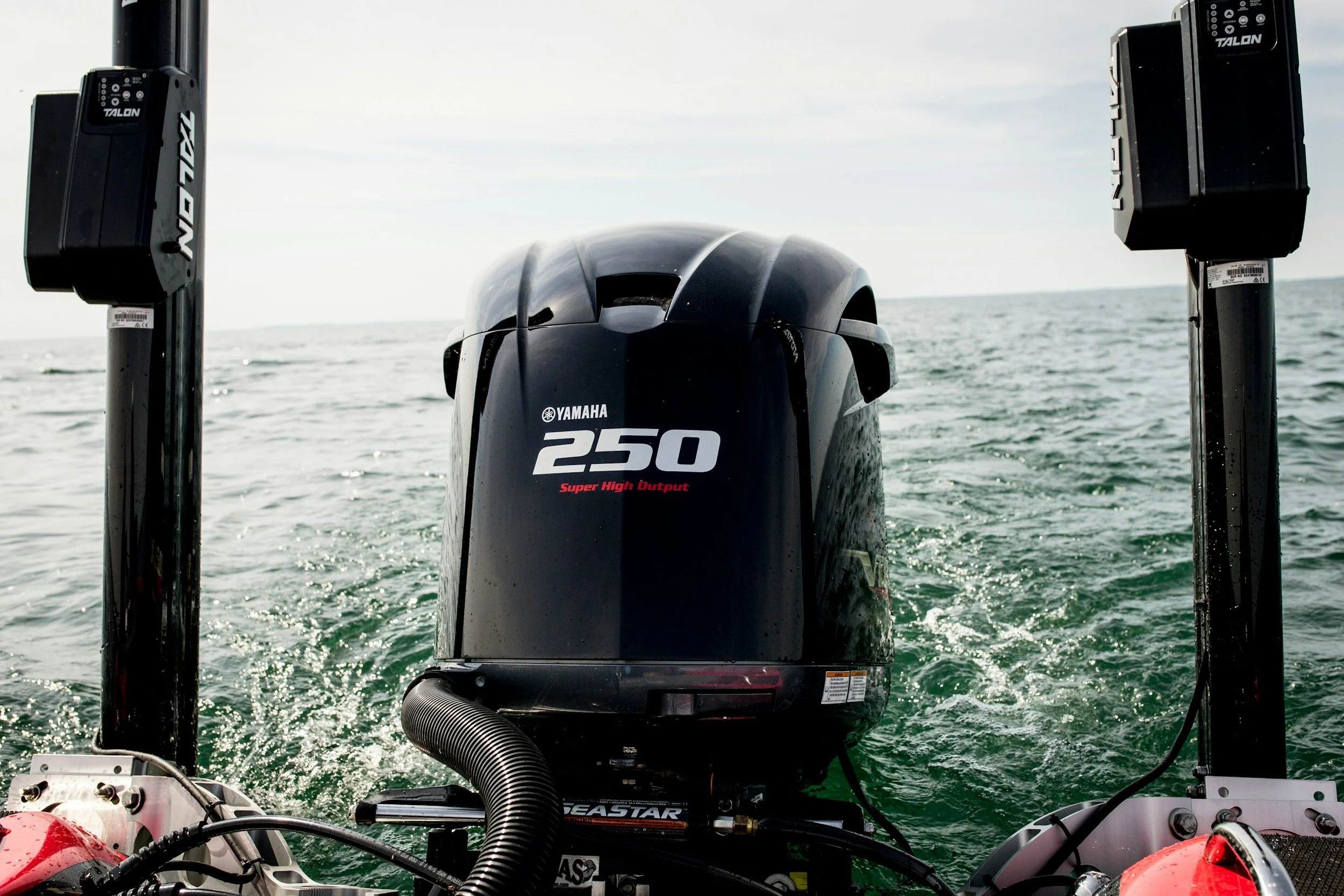 View of a Yamaha 250 outboard motor on a boat, with the ocean and a partly cloudy sky in the background, and part of a red life jacket and boat equipment visible in the foreground.