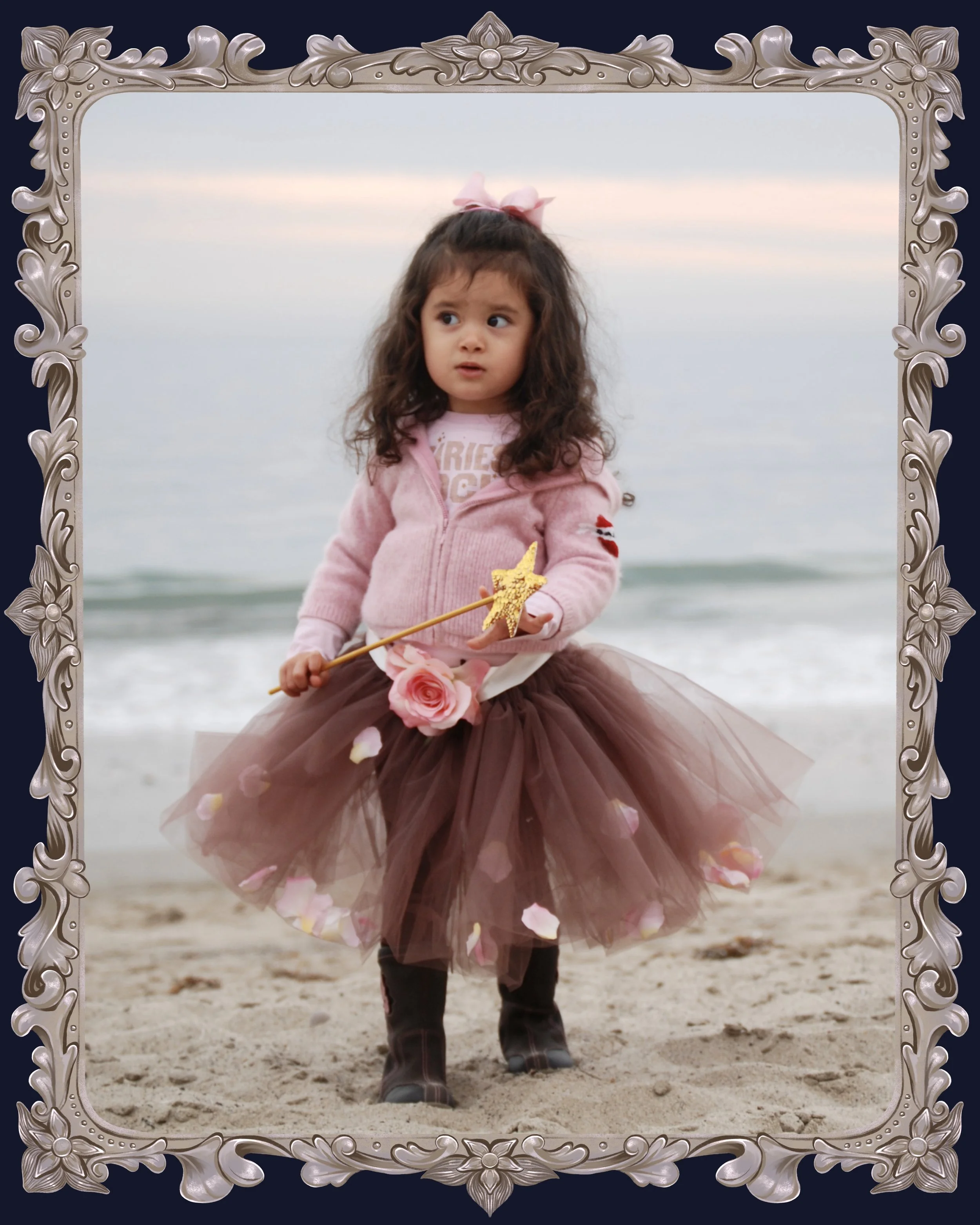 Photo of children's book author and illustrator Anabelle Rottman as a toddler. She is shown at the beach holding a magic wand and wearing a puffy pink tutu covered in rose petals.