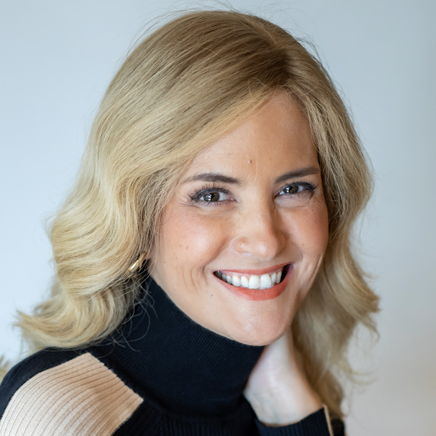 A woman with blonde hair smiling at the camera, wearing a black turtleneck sweater with beige accents.