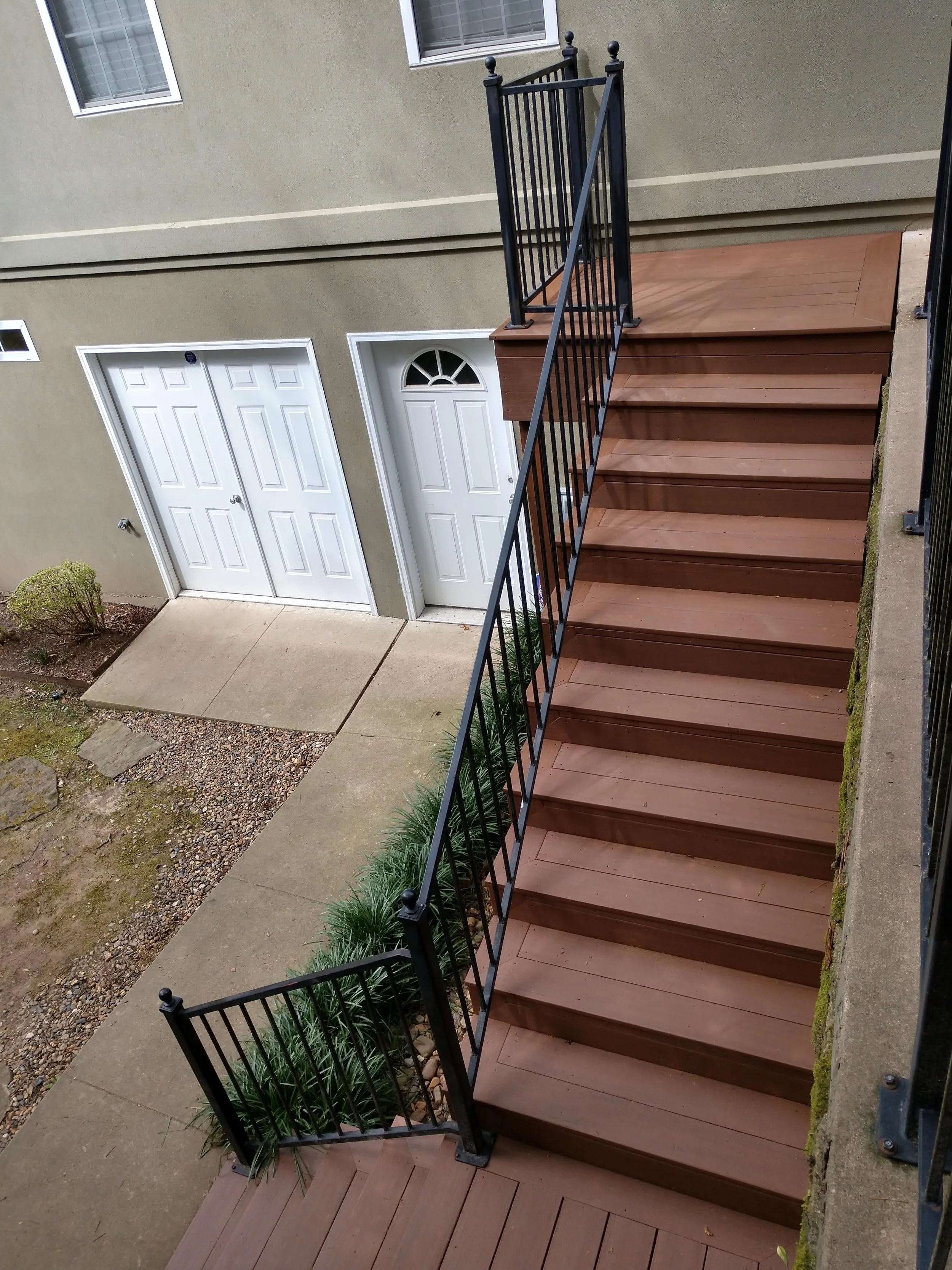 Wooden outdoor stairs with black metal railing leading up to a beige building with two white doors and two small windows.