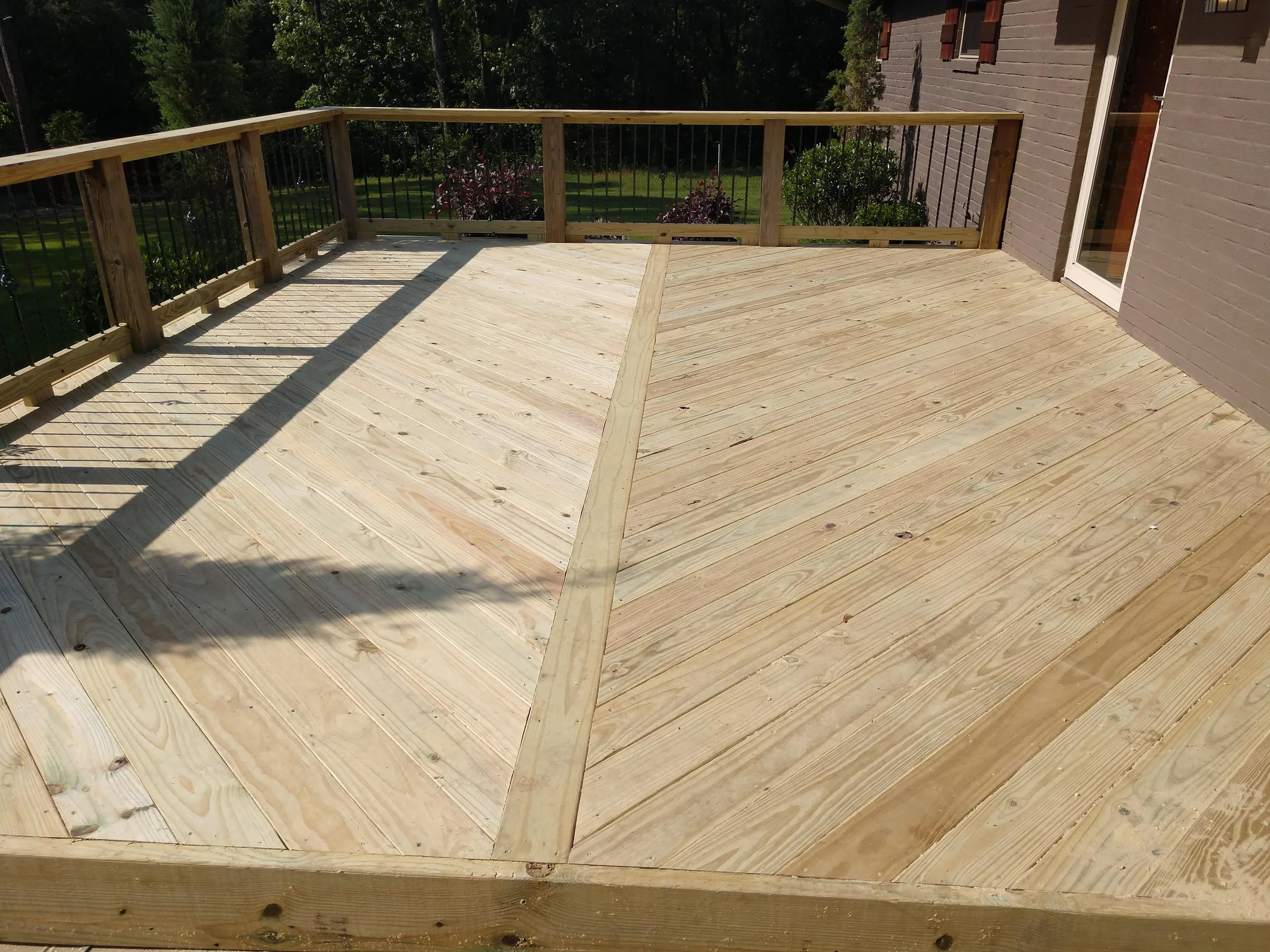A newly built wooden deck attached to a house, with a railing and view of a backyard with grass and trees.