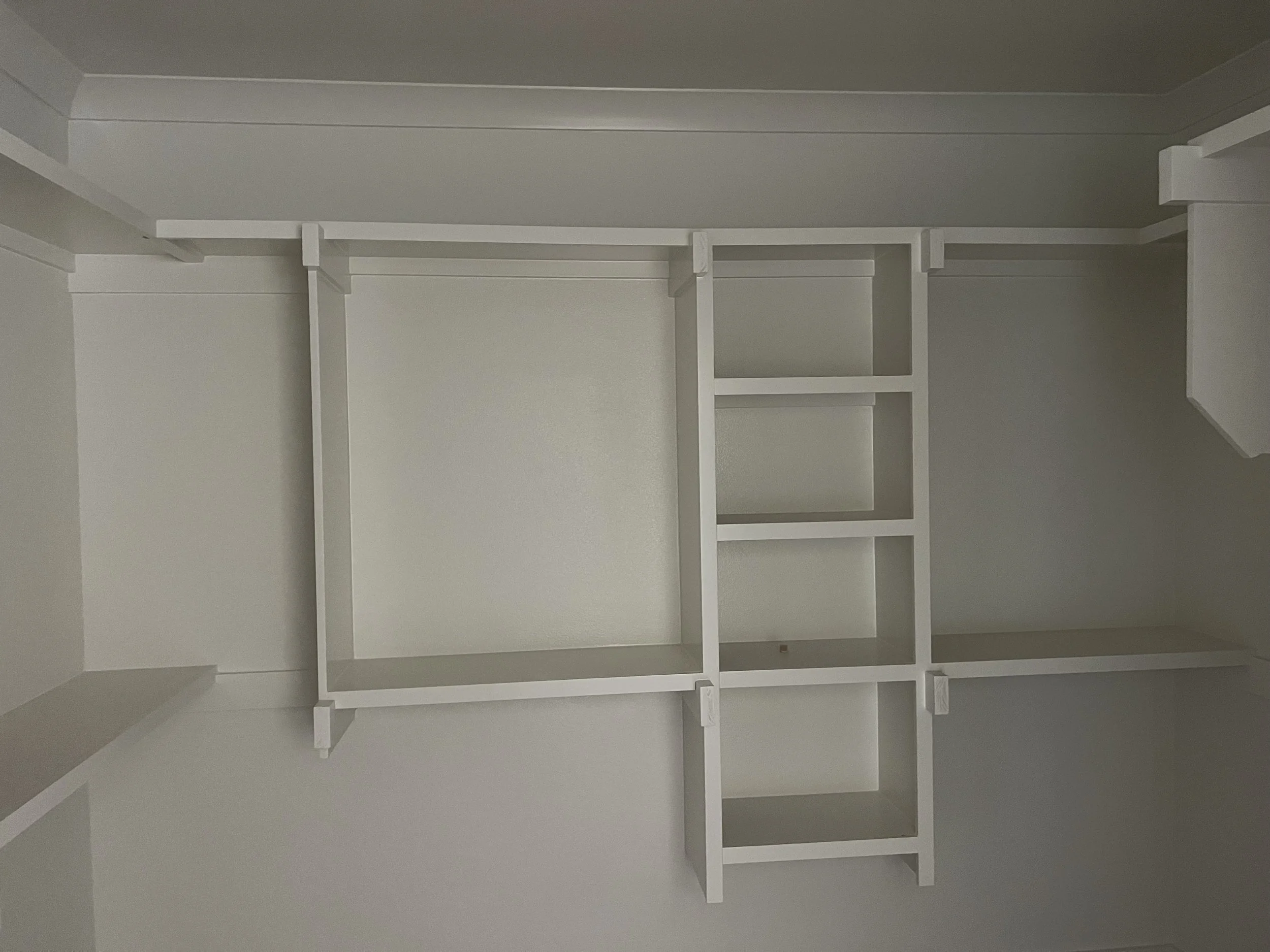 Empty white built-in closet with multiple shelves and a hanging rod against a white wall.