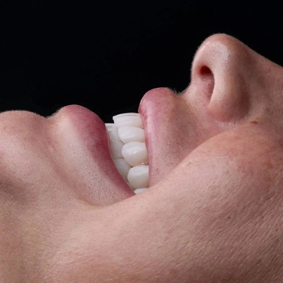 Close-up of a person biting into a white chocolate bar against a black background.