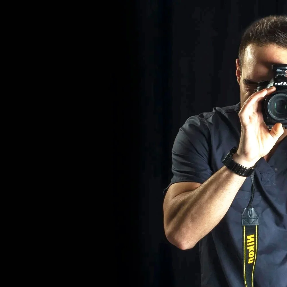 Photographer taking a picture with a Nikon camera toward a black background.