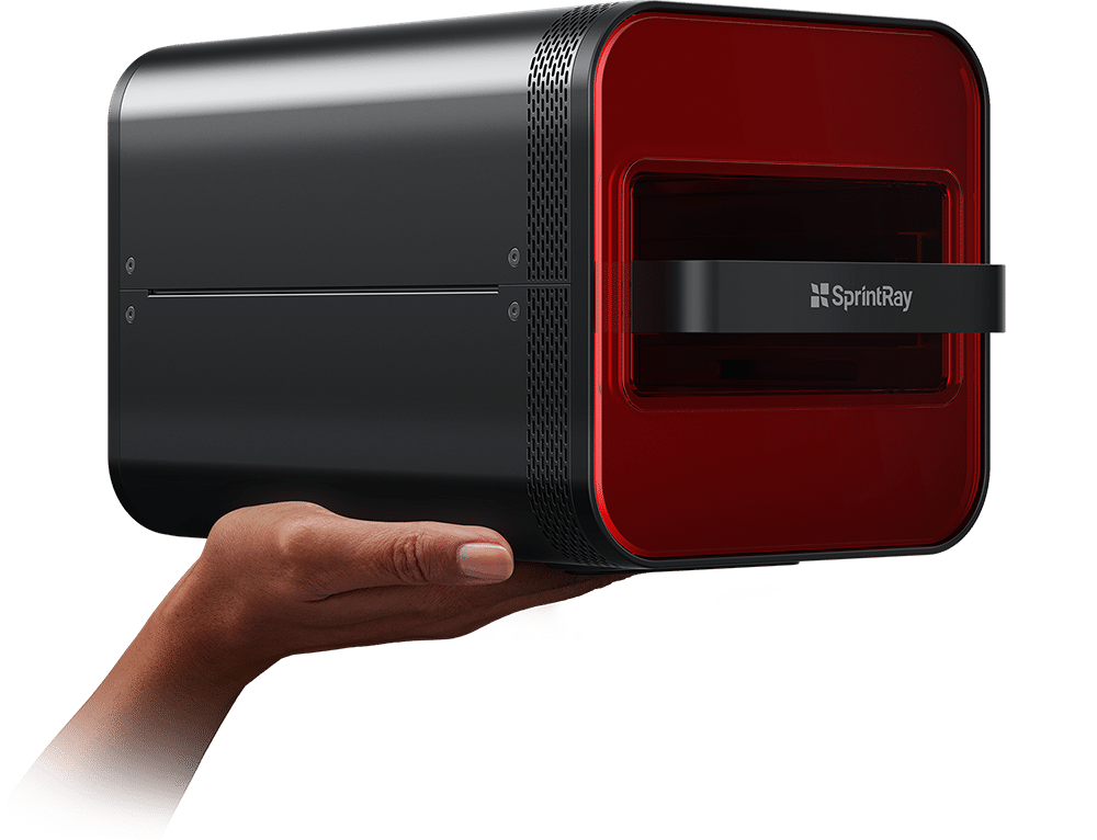 A hand holding a compact, black and red industrial 3D printer or laser scanner labeled 'SprintRay'.