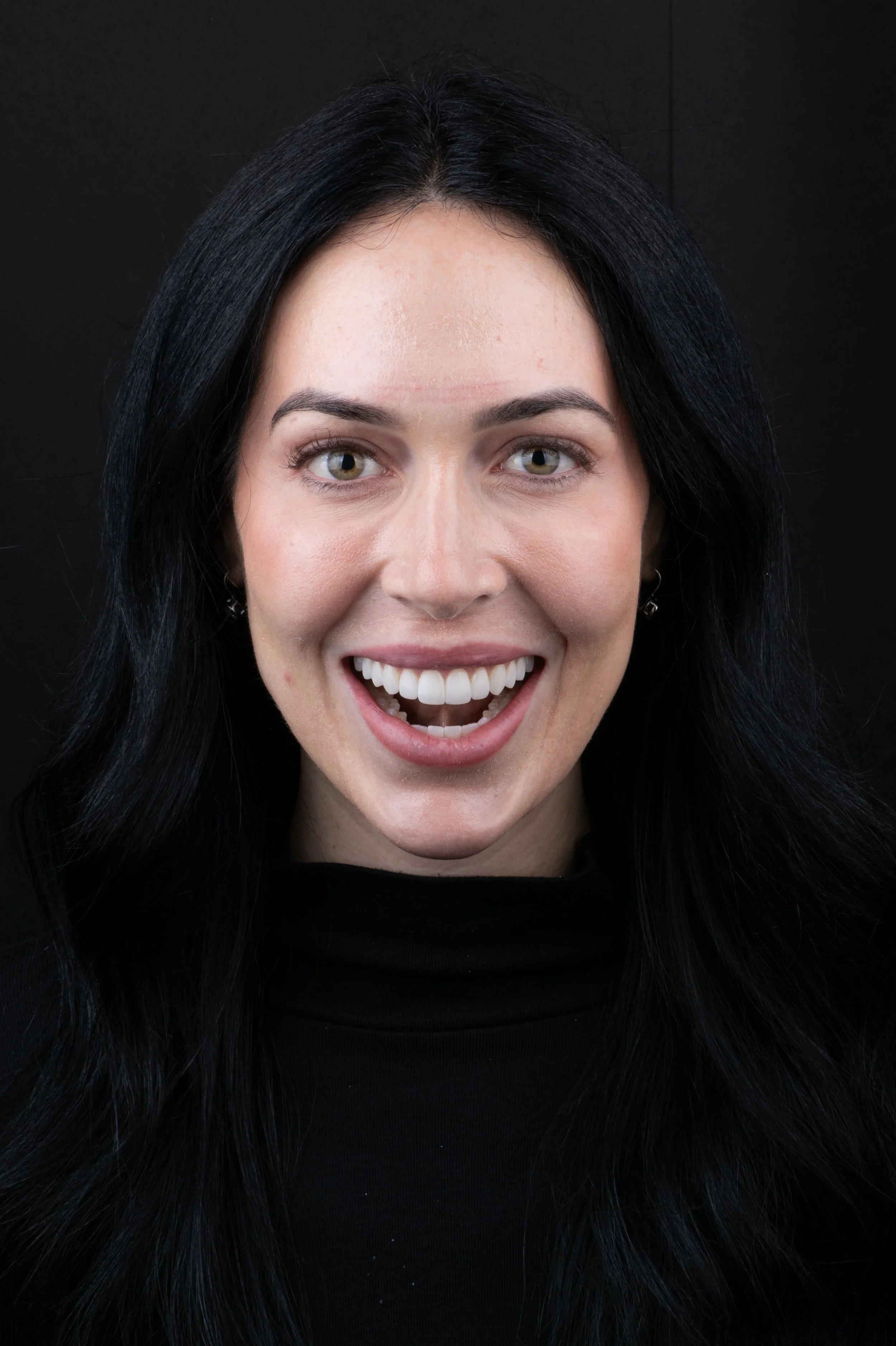 Close-up of a woman with long black hair, smiling widely, against a black background.