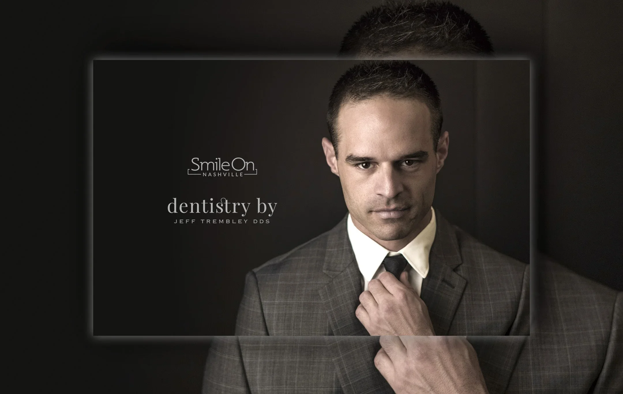 A man in a checked suit and tie adjusting his collar while looking directly at the camera. The image appears to be a promotional or professional portrait with a dark background.